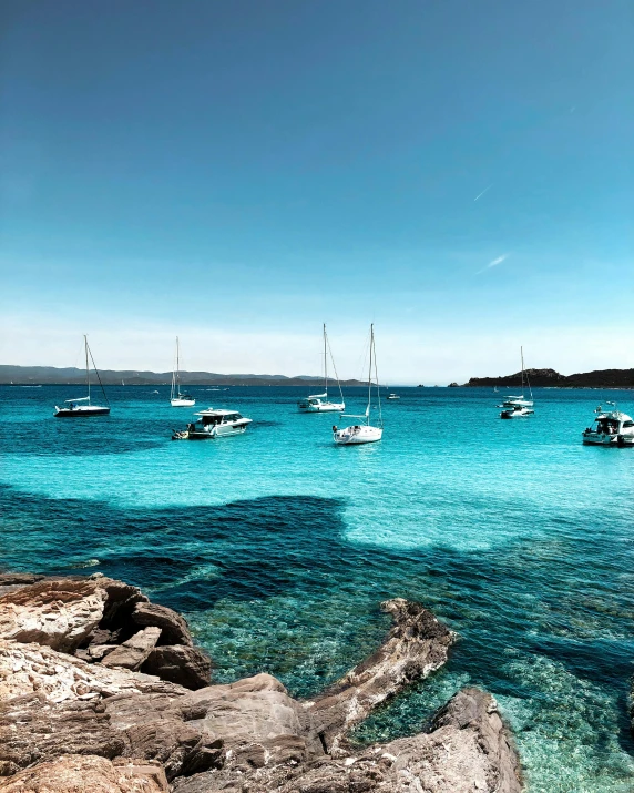 many boats floating in the blue water near the rocks