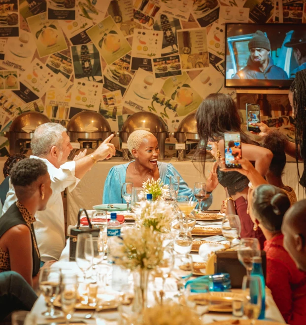 the large group of people are sitting at a table in front of the television screen