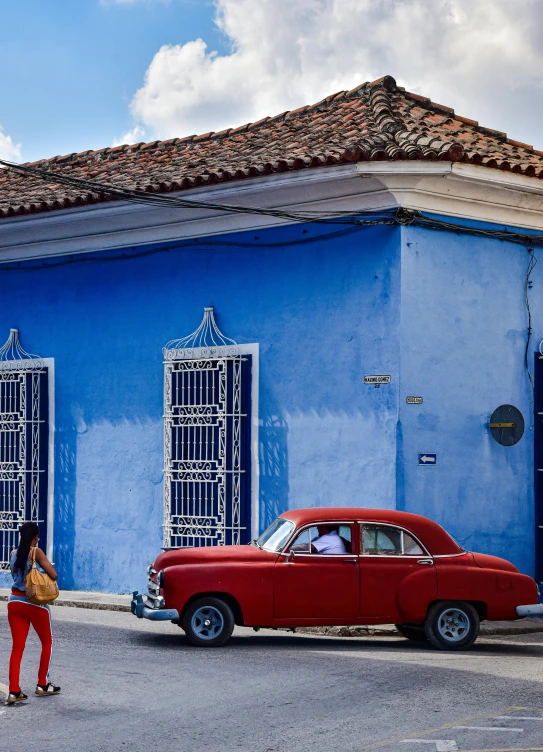 an old red car parked in front of a blue house