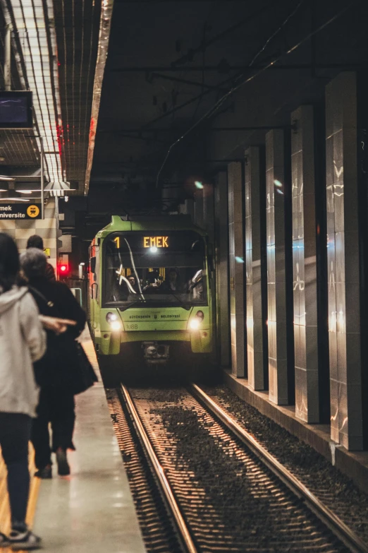 some people walk towards a green train in the dark