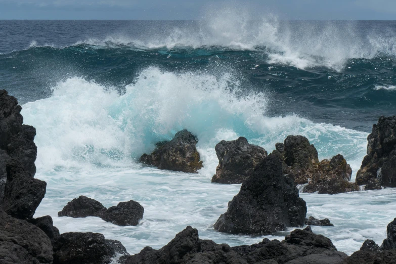 the water is splashing on rocks and wave crashes into the shore