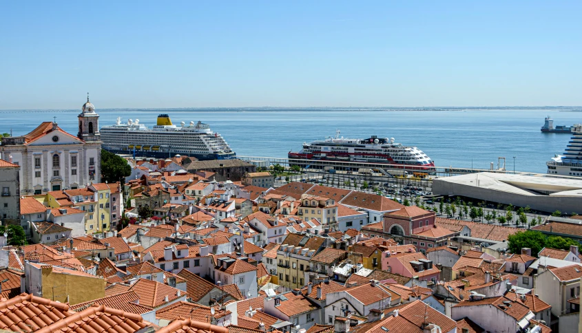 a red roof tops looks like a village with a cruise ship docked in the background