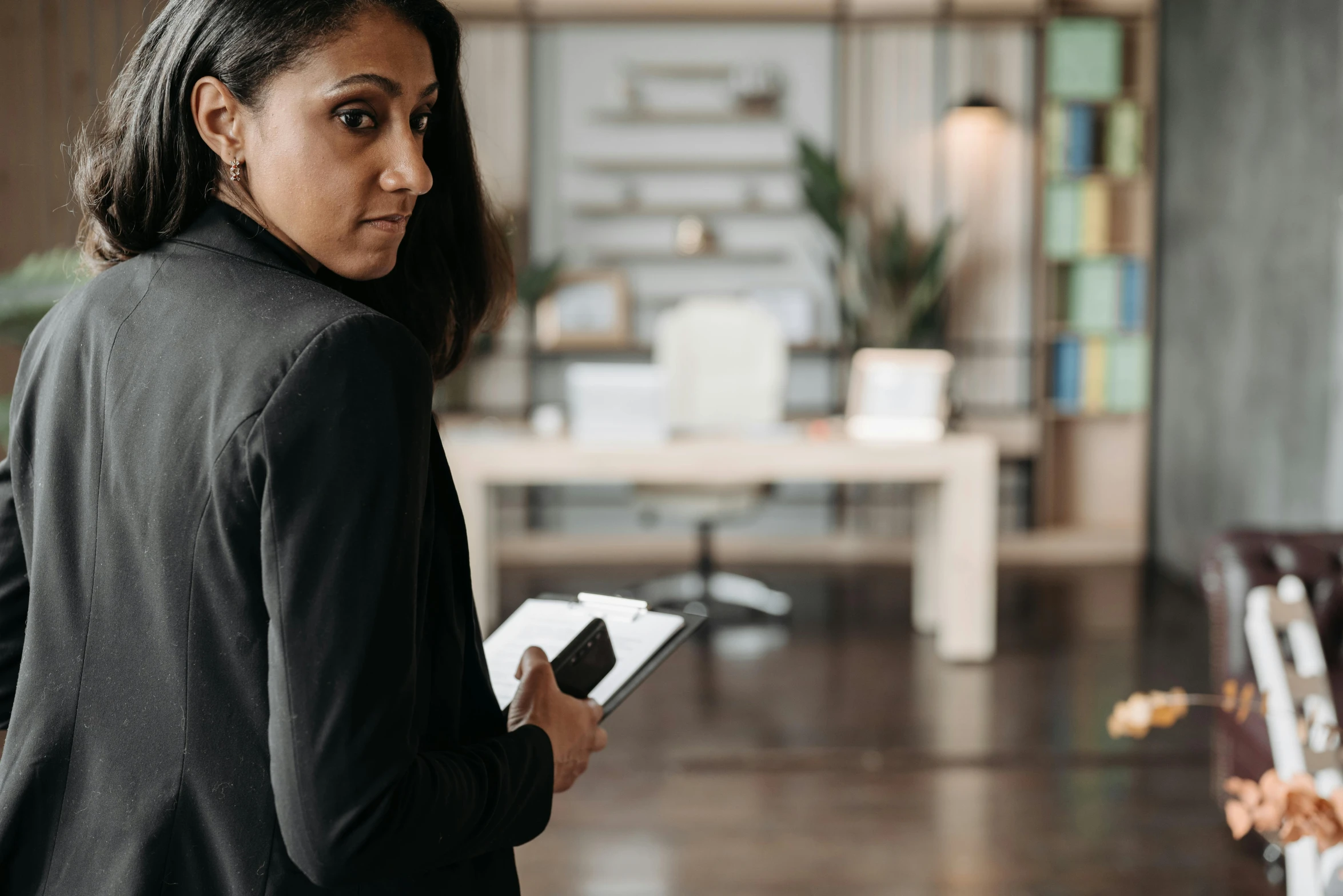 a woman with a black blazer holding a piece of paper and talking to someone