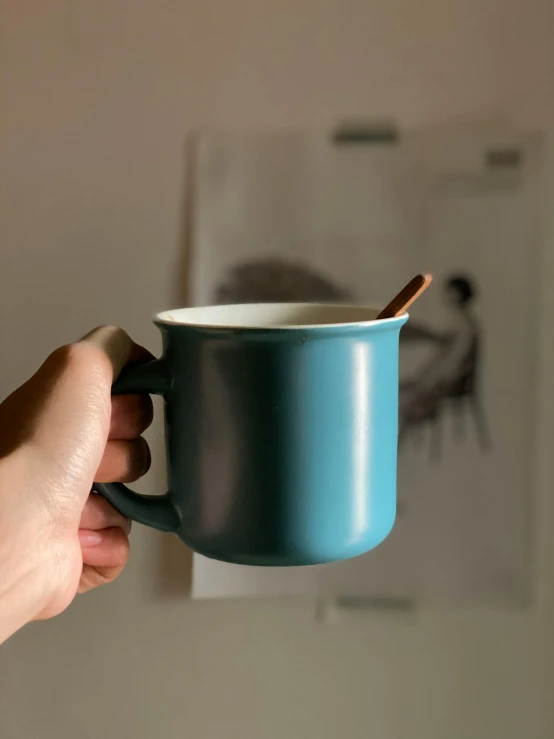 a hand holding a coffee cup with a spoon in it