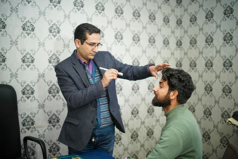 a man in glasses and a sweater brushing another mans hair