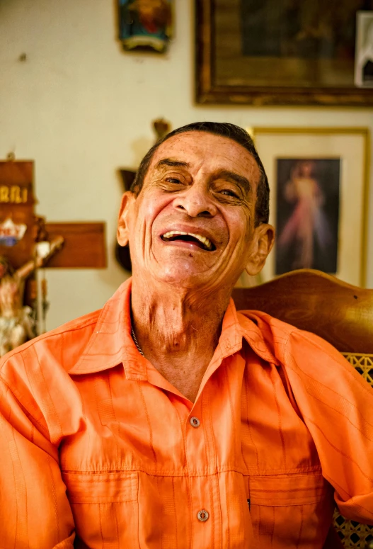 an older man smiles in an orange shirt