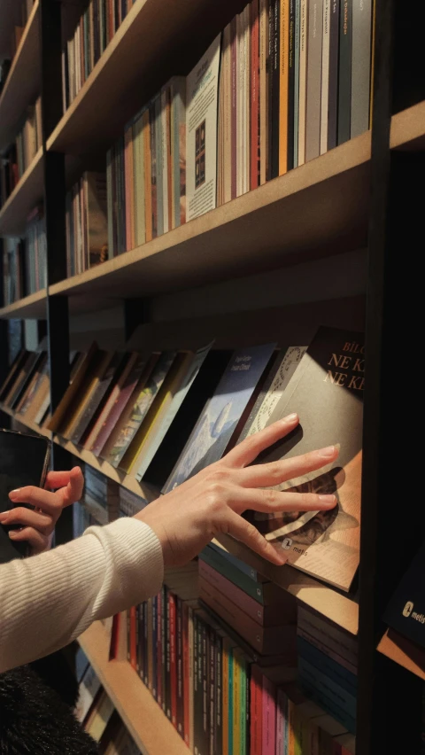 a person that is reaching for books on a shelf