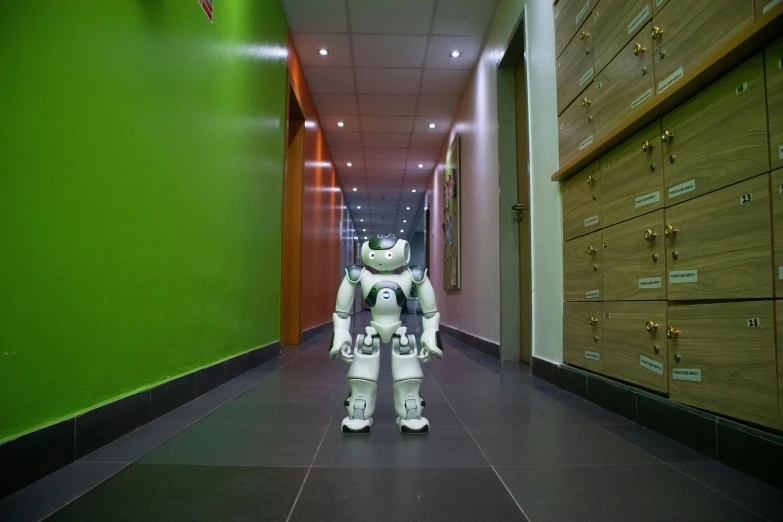 a robot stands in an office hallway while looking at some drawers