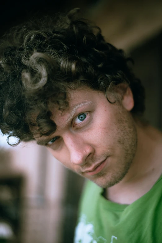 a man with curly hair wearing a green shirt looking off to the side