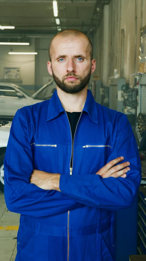 man with beard and blue work jacket stands in garage