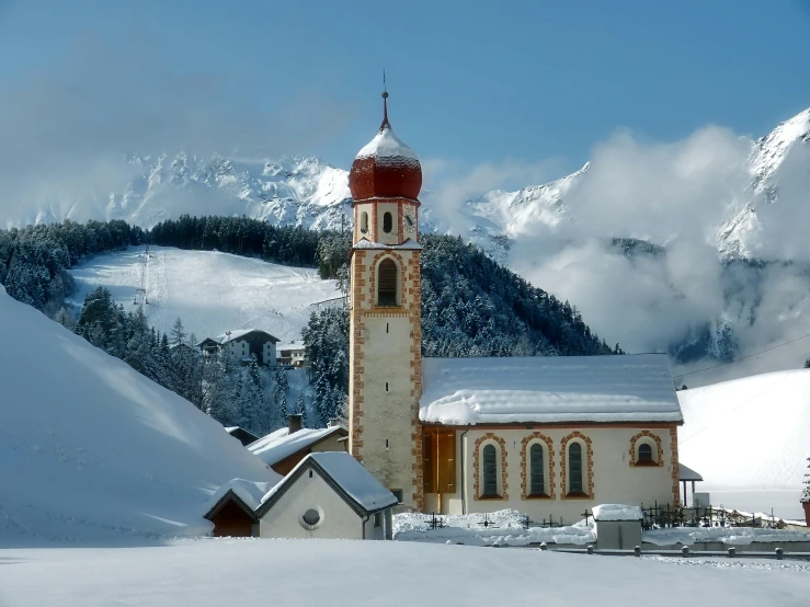 a small church with a tall tower is covered in snow