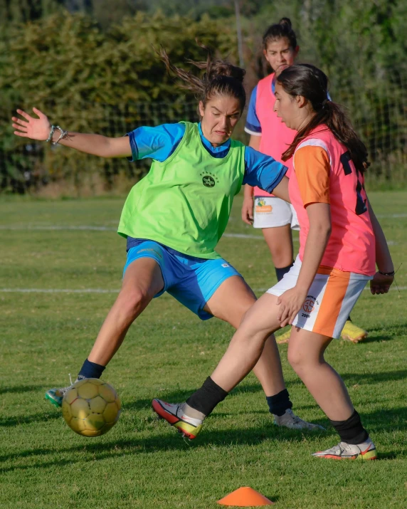 a group of girls in a grassy field kicking around a soccer ball