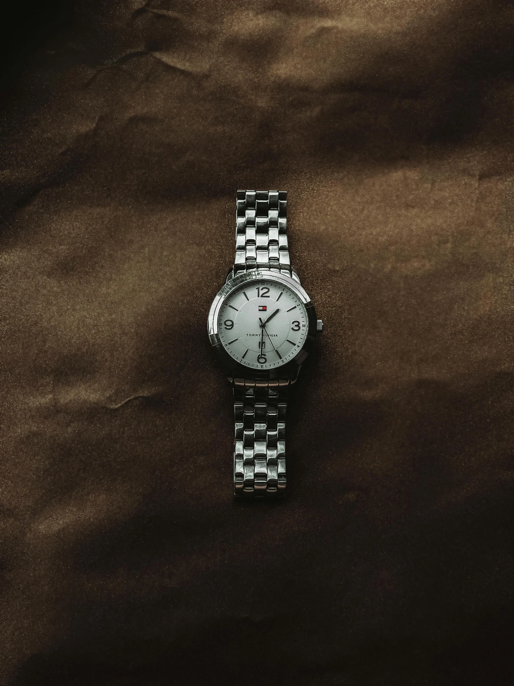 a woman's silver watch sitting on a brown surface