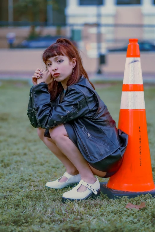 a woman sitting next to a traffic cone on the grass