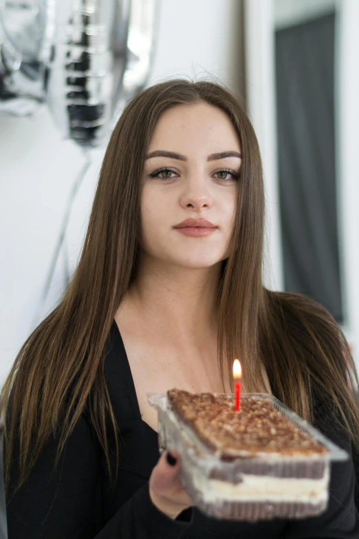 a woman holding a piece of cake with a candle on top