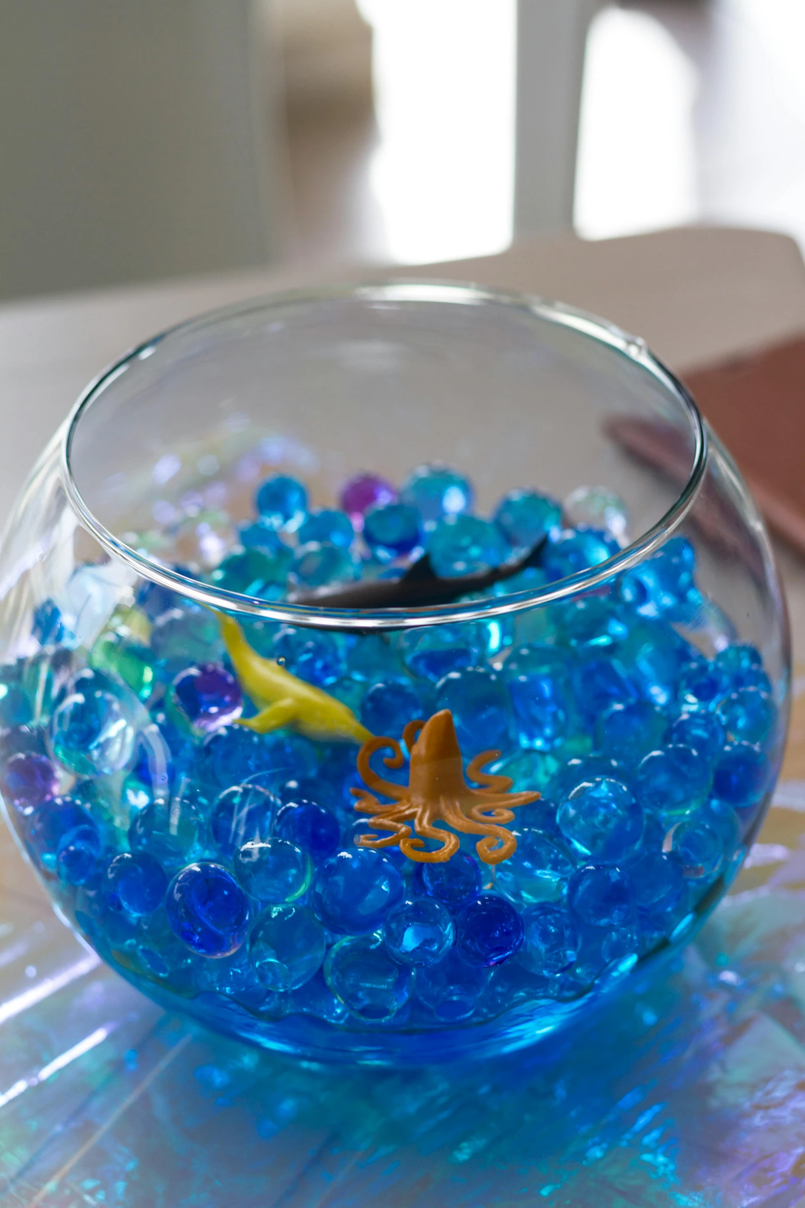 a bowl filled with blue beads and a fish on a table