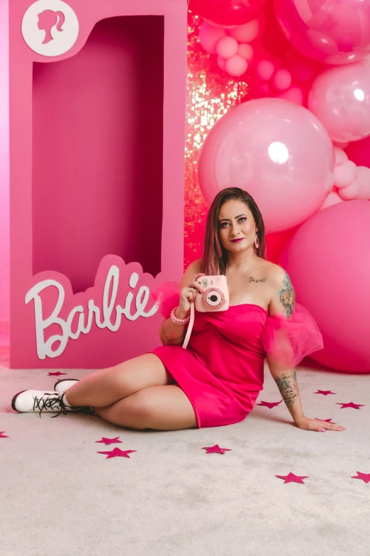 a beautiful woman sitting next to a pink barbie birthday decoration