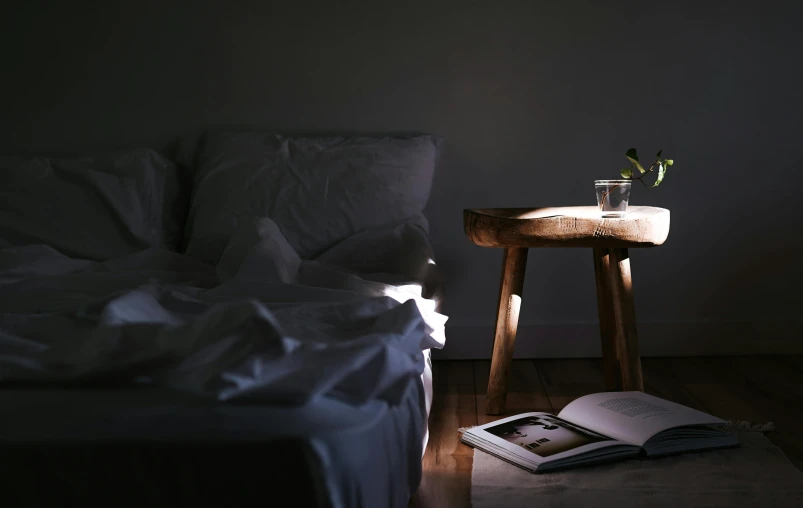 an empty bed and nightstand with book in the dark