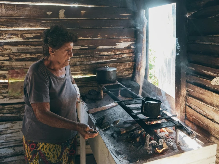 an old woman cooking on a stove in a log cabin