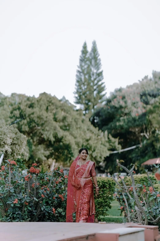 a woman wearing a red sari and standing in front of some trees