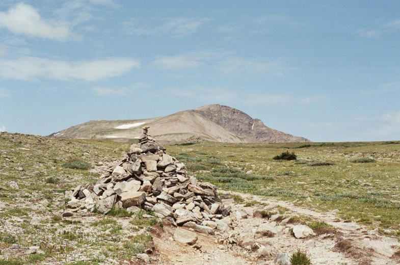 a pile of rocks in a grassy field with a mountain in the background