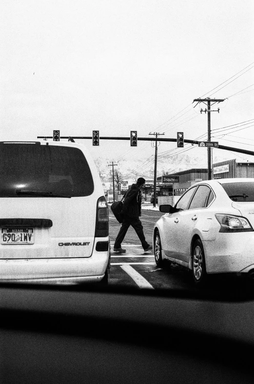 a man walking across a crosswalk near parked cars