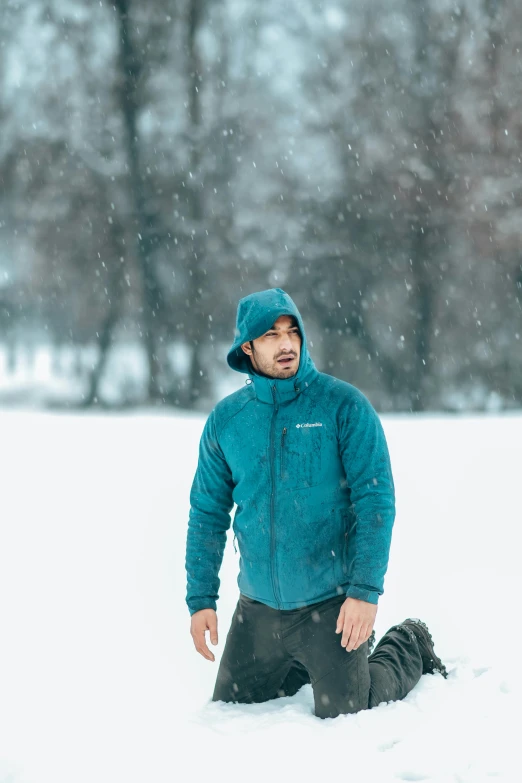 man in cold clothing crouching down while falling into the snow