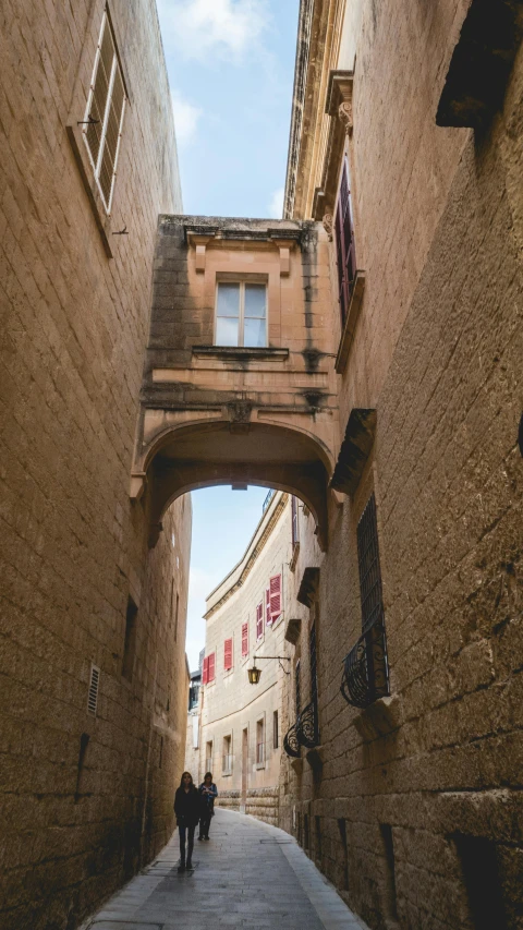 two people are walking under a bridge on a narrow street