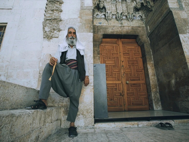 an old man in black and white is leaning on a stone wall with a cane