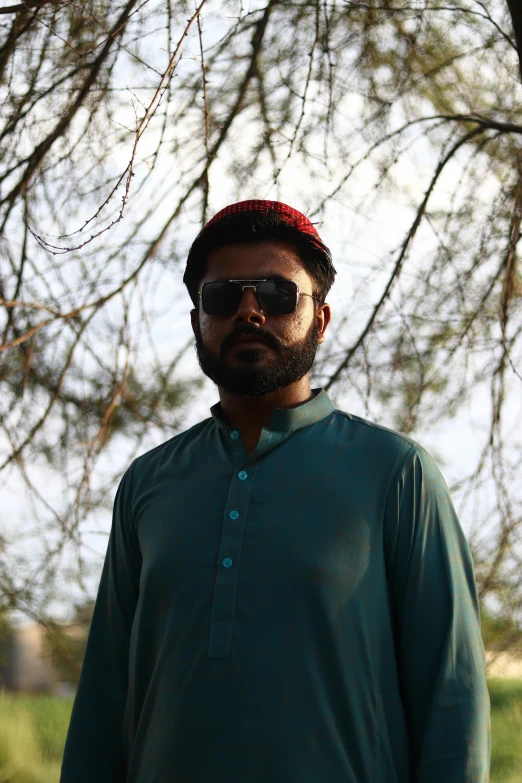 a man wearing sunglasses and a hat standing under a tree