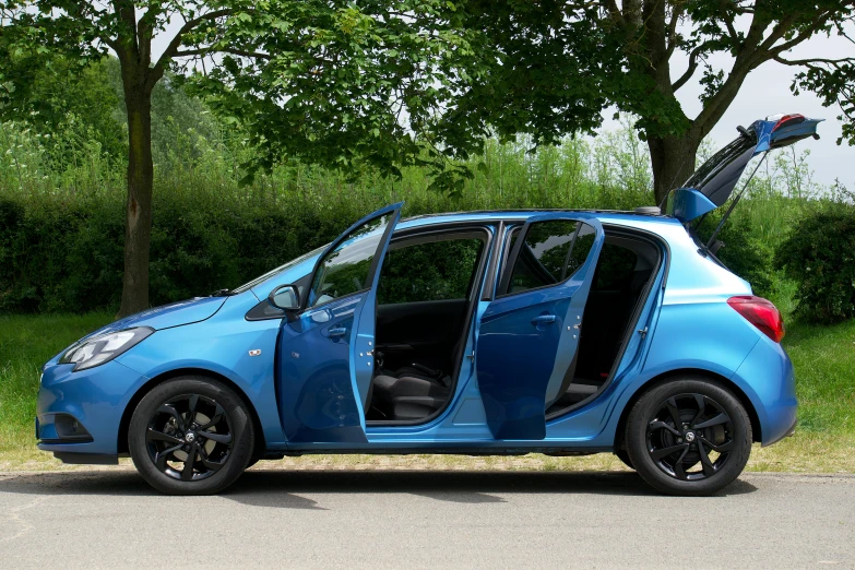 a blue smart car with it's door open in front of a bunch of trees