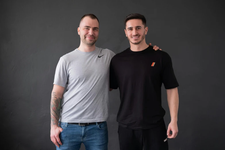 two men pose for the camera with a black background