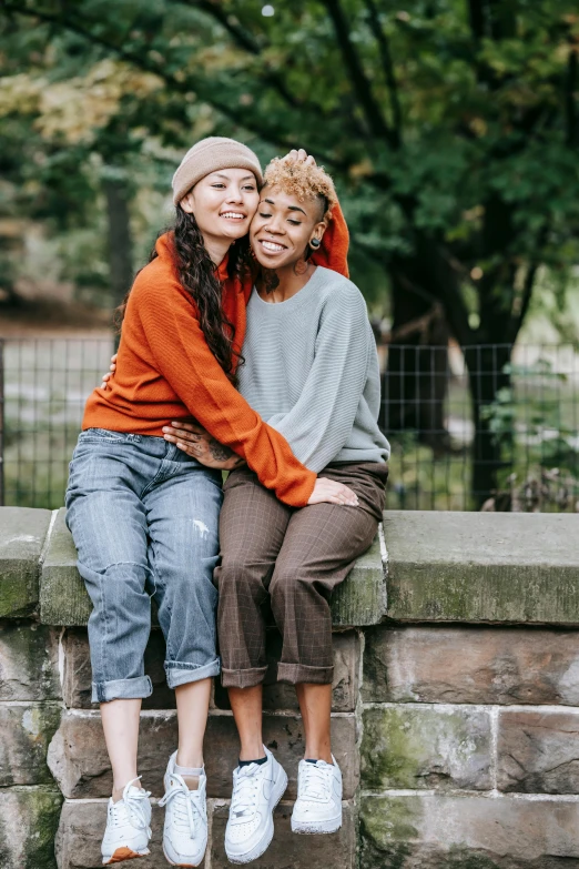 two women sitting on a cement block in front of some trees