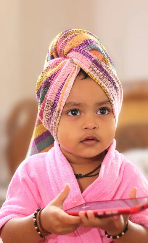 a young child with a colorful towel on her head looking at a tablet