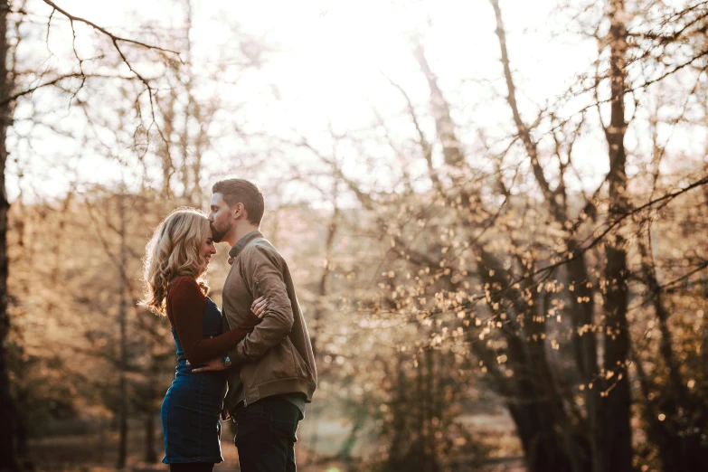 a young couple hugging in the woods with trees in the background