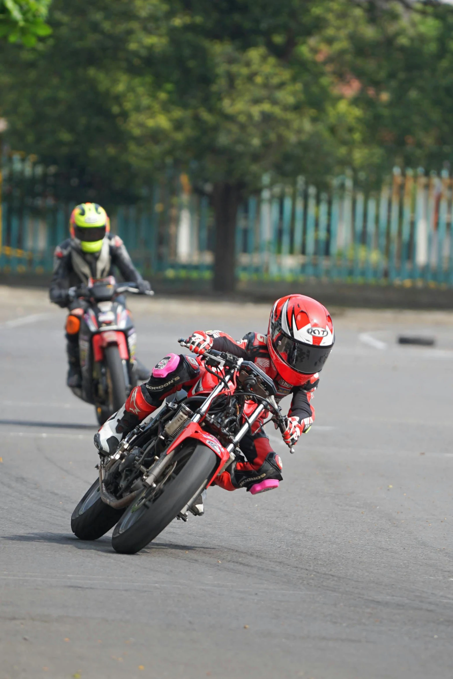 two motorcyclists in a red and black outfit driving in the middle of a road