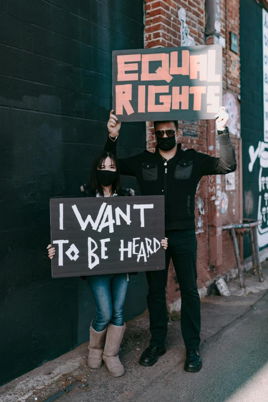 two people stand outside holding protest signs