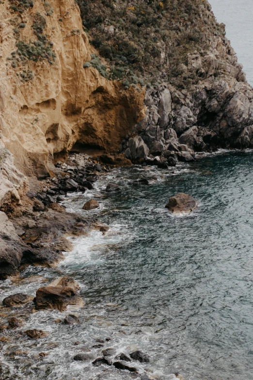 the cliff side of a mountain overlooking the ocean with a bird flying over the water