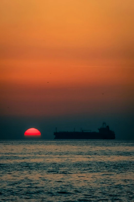 a sunset over a large cargo ship in the distance