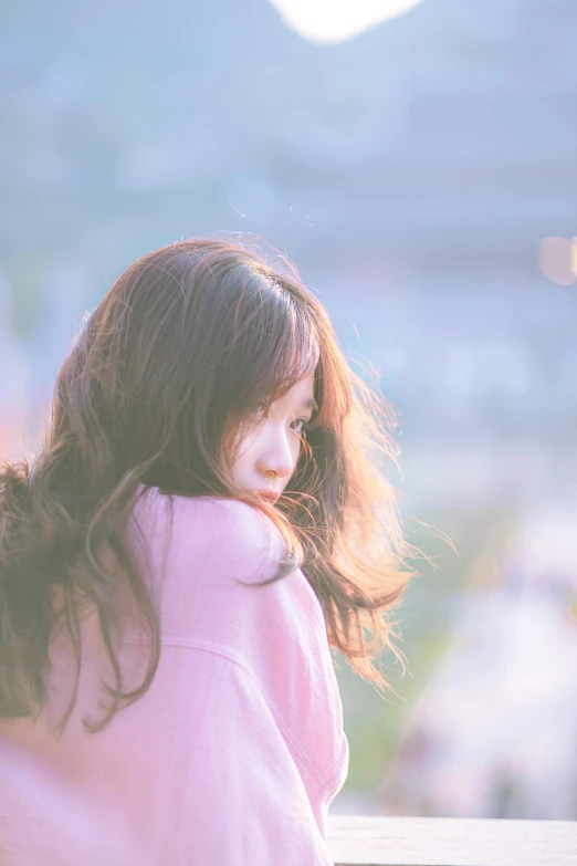 a girl wearing pink sits on a bench with her hair flowing