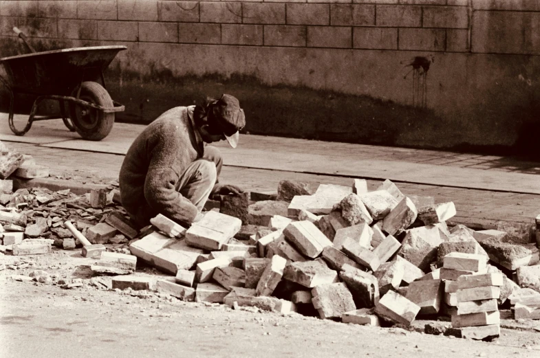 an old man standing over piles of bricks next to a wheelbarrow