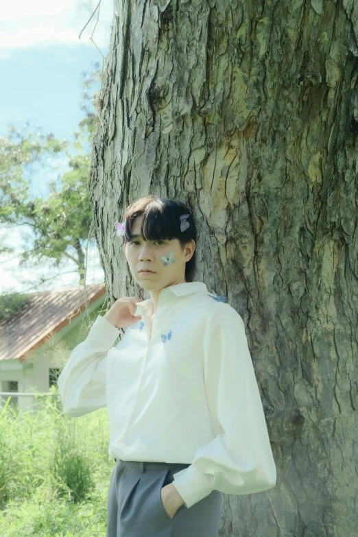 a woman leaning against a tree while wearing ear clips