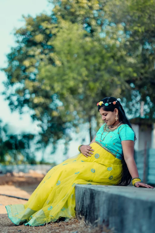 a woman in a green sari, sitting on concrete