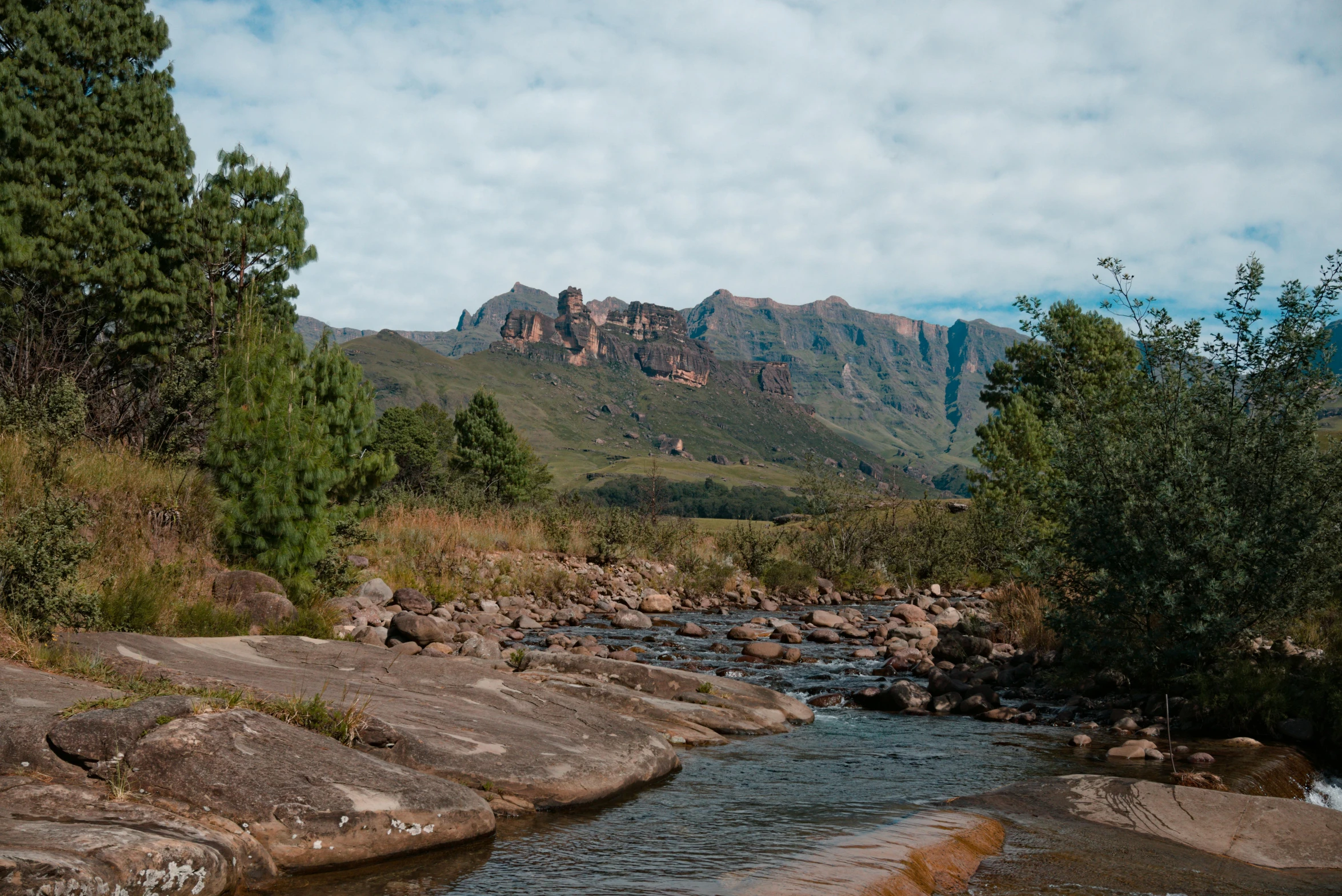 a river in between some green mountains under cloudy skies