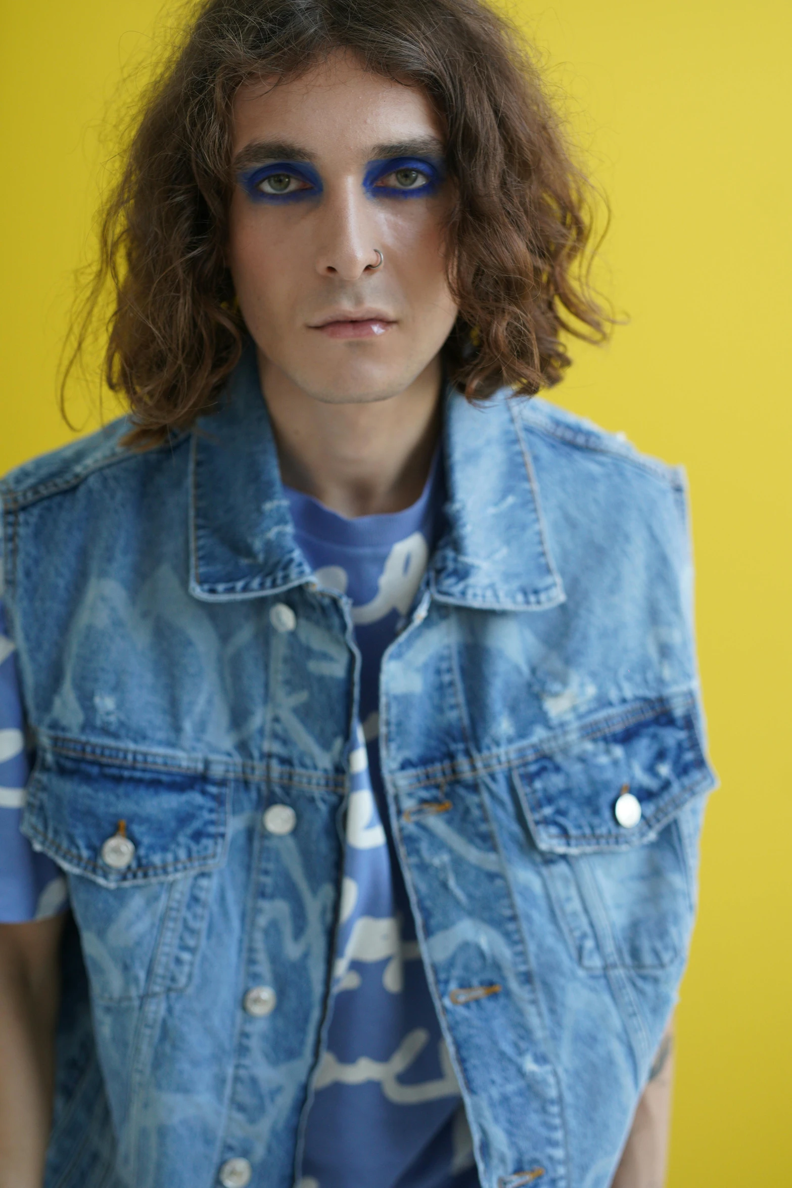 man with blue eyeliner wearing a denim vest and shirt