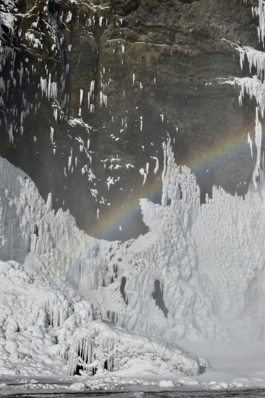 a rainbow shines behind some ice covered mountains