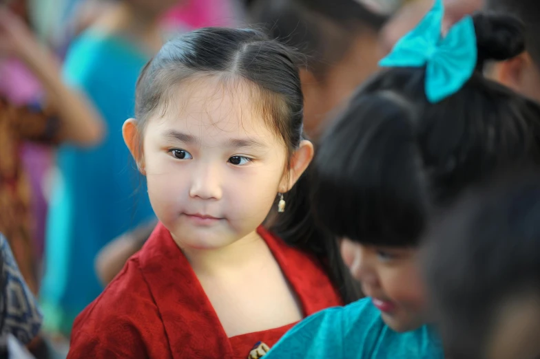 an asian girl looks towards the camera with many other children behind her