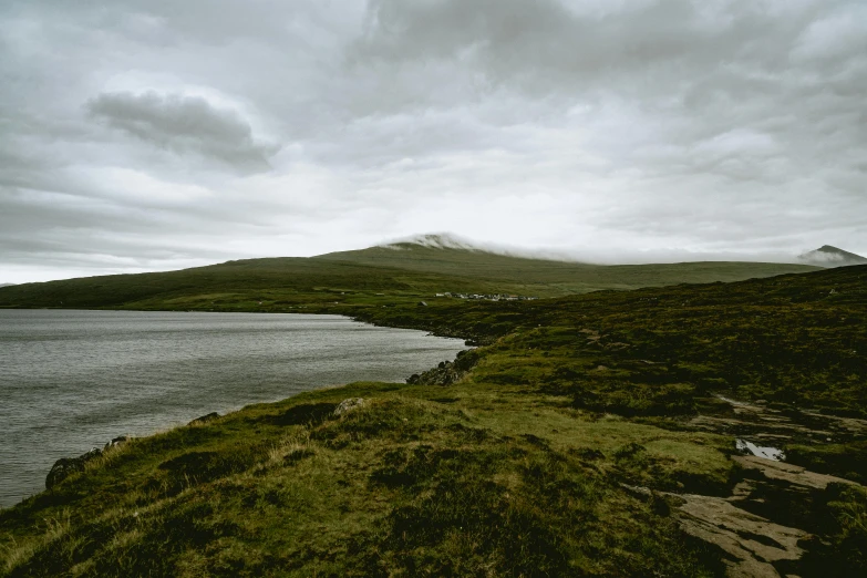 the body of water on a cloudy day next to a hill