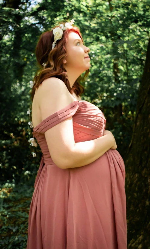 a pregnant woman in a dress is standing under trees