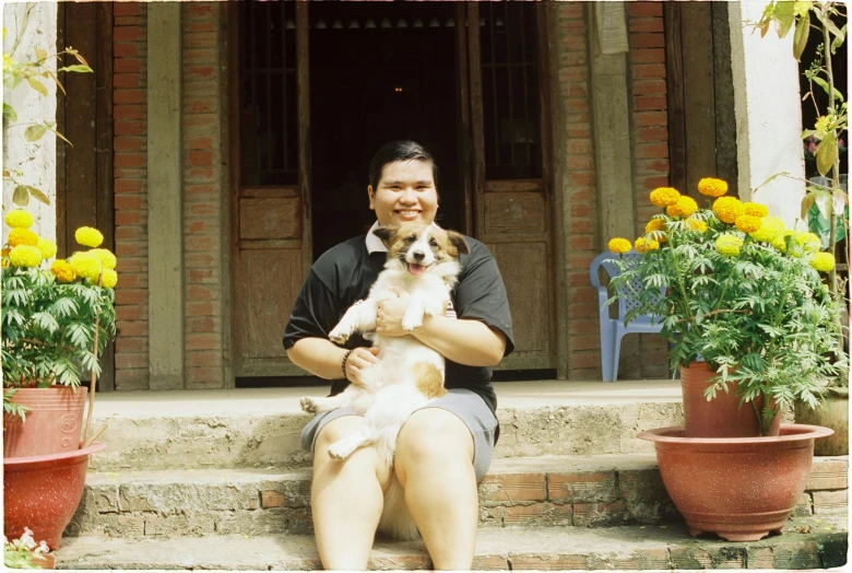 a man holding a dog on his lap near flower pots